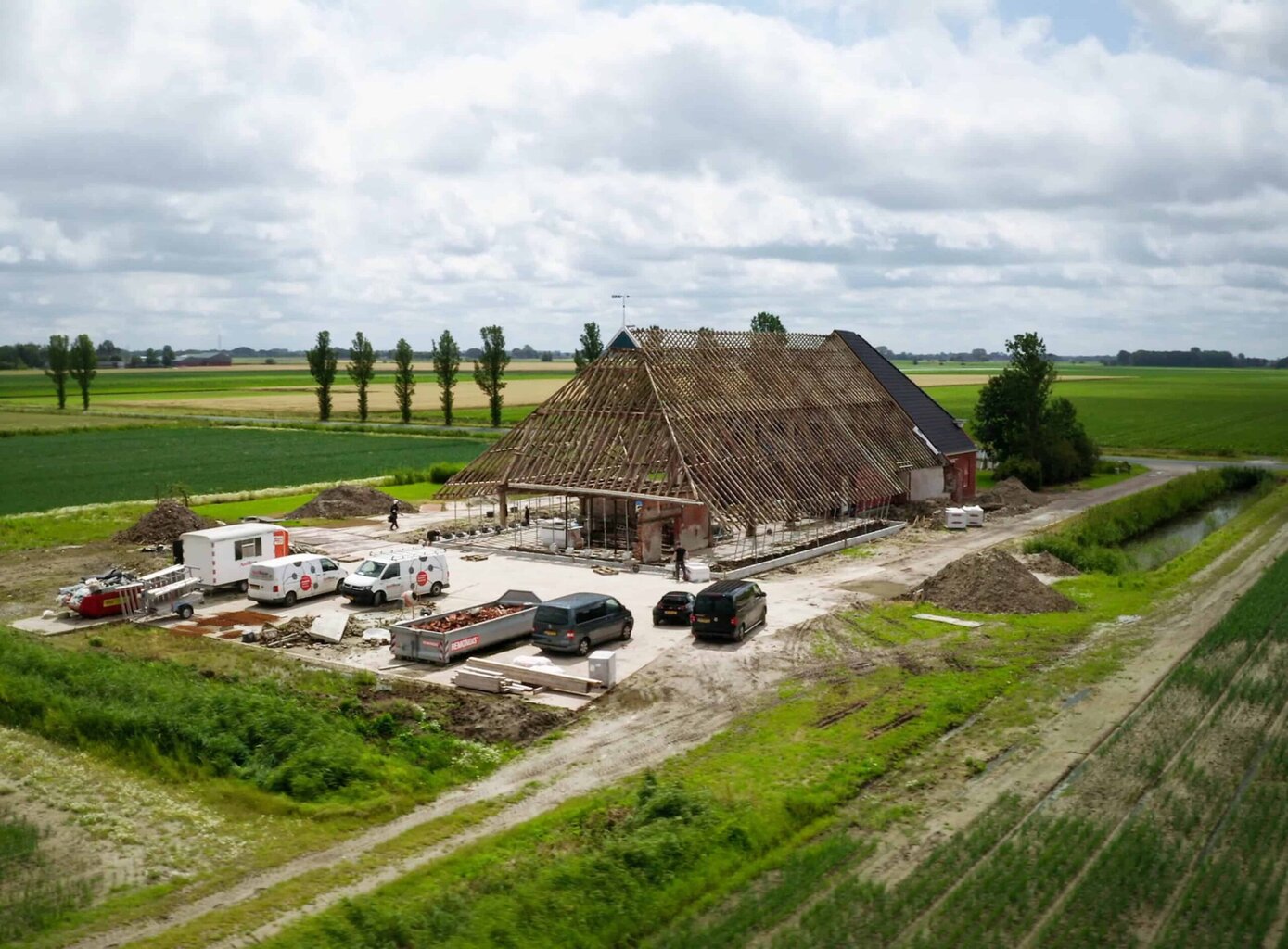 Onontwikkeld boerderijgebouw onder constructie op het platteland met groene velden en een heldere lucht.